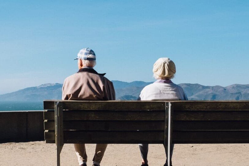 pareja de espaldas sentados en un banco mirando al mar