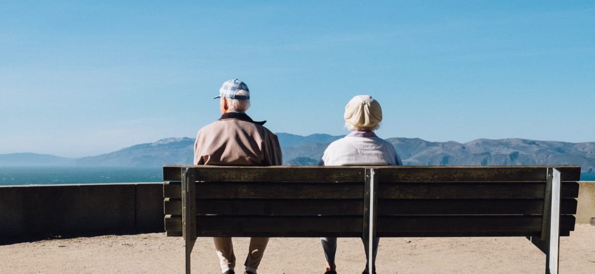 pareja de espaldas sentados en un banco mirando al mar