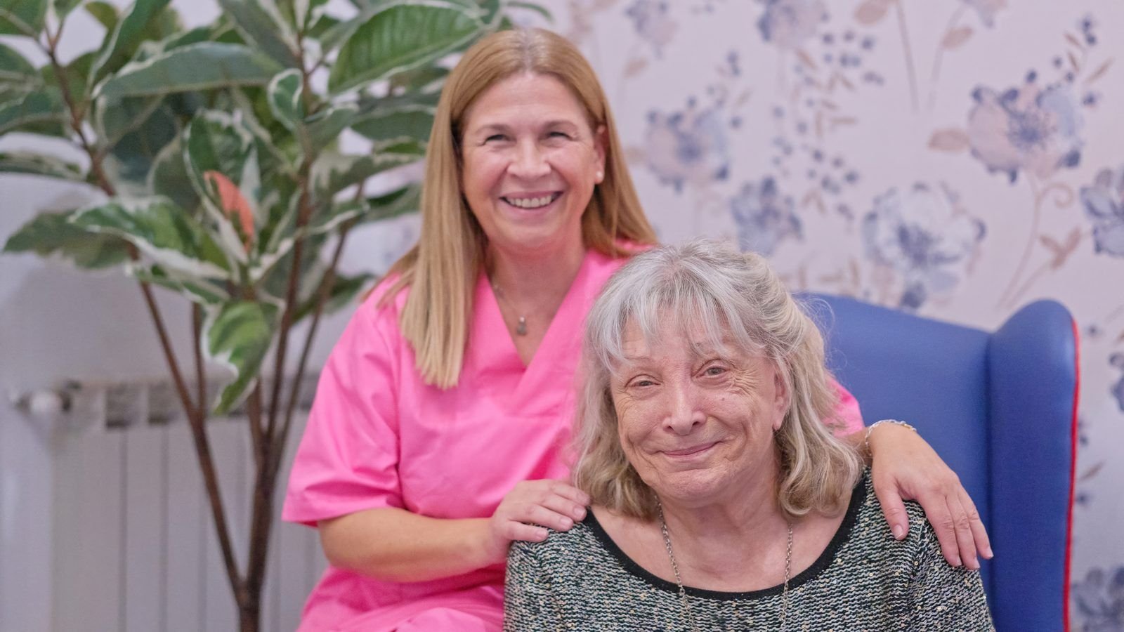 Cuidadora y señora mayor sonriendo juntas en el sofá